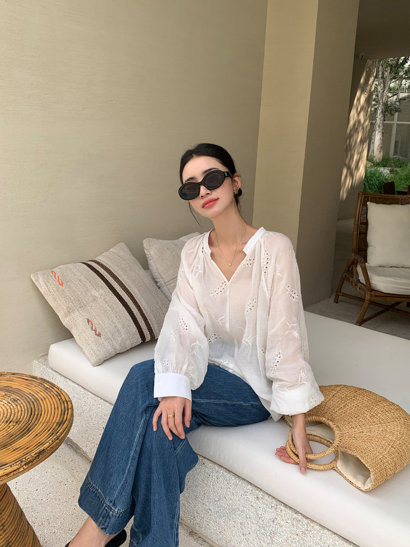 Woman wearing a white embroidered blouse with blue jeans and black sunglasses