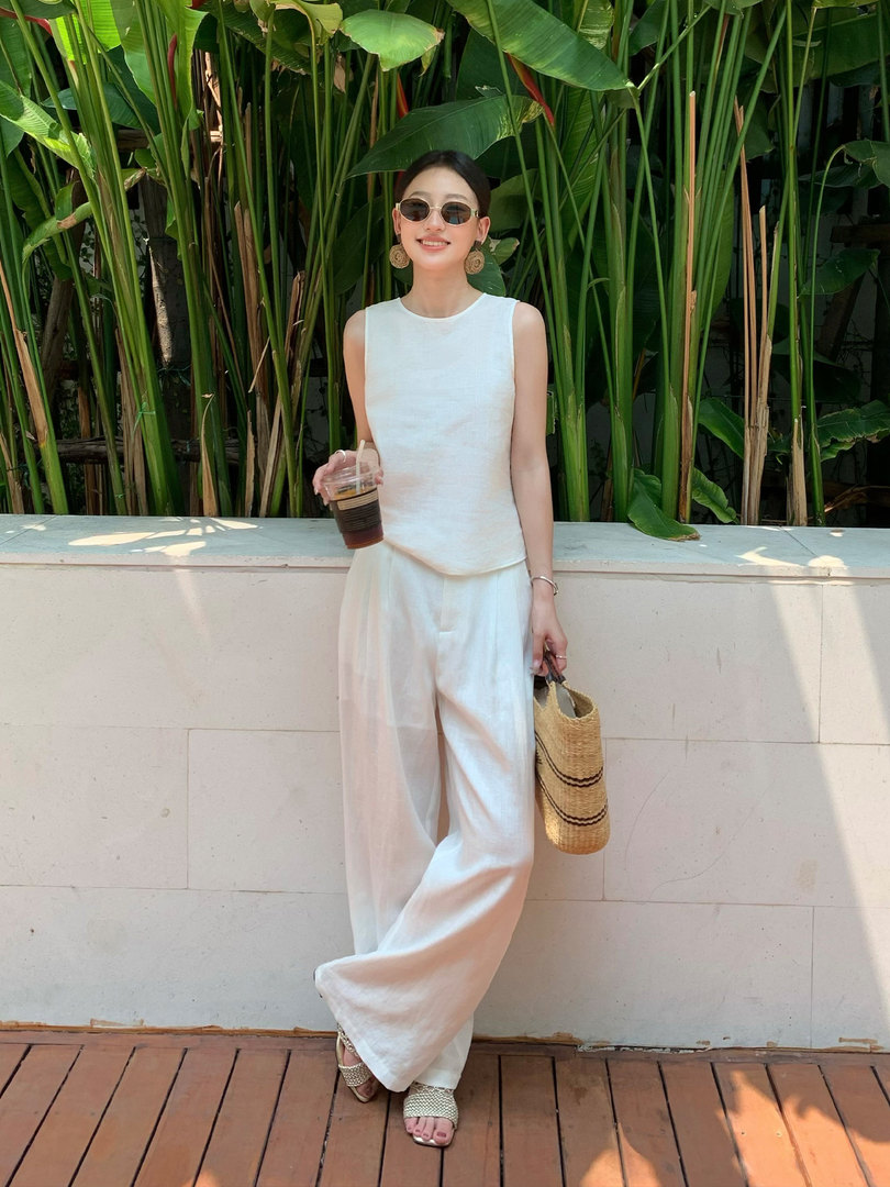 Woman wearing a white sleeveless top and wide-leg pants with a straw bag outdoors