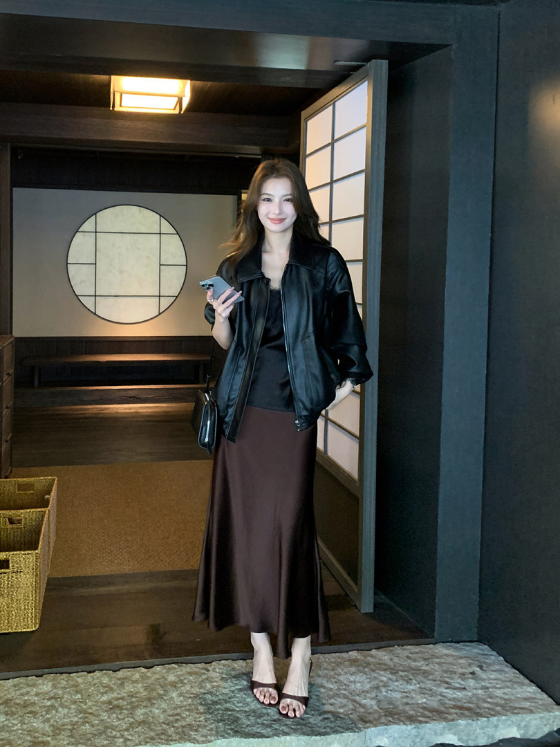 Woman wearing a black jacket with a long brown skirt in an indoor setting