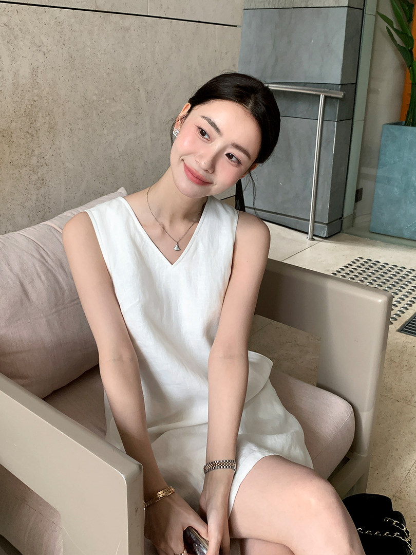 White sleeveless V-neck dress worn by a seated model