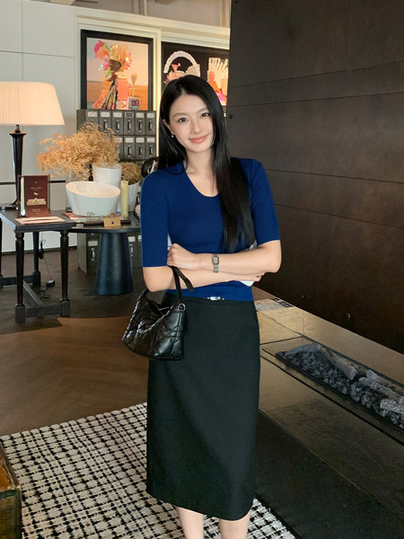 Woman wearing a blue fitted top and black skirt with a black handbag