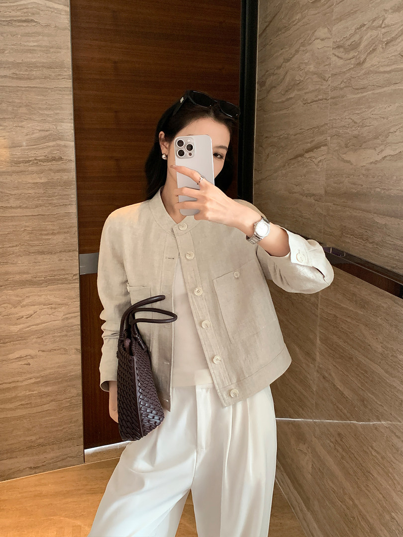 Woman wearing a beige button-up jacket with white pants and a woven handbag