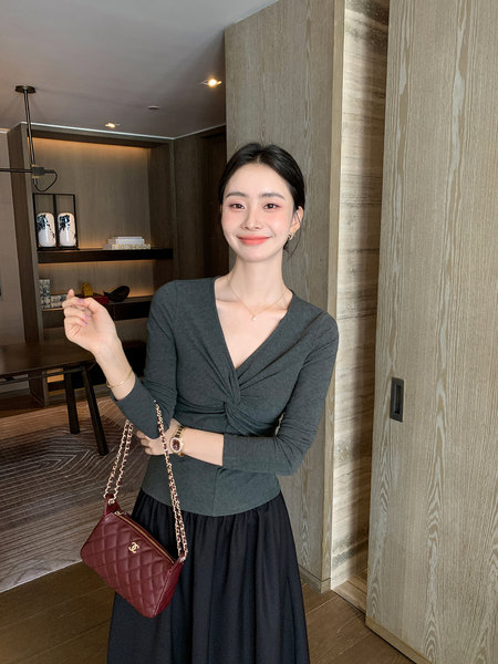 Woman wearing a dark fitted top and long black skirt while holding a burgundy chain-strap handbag
