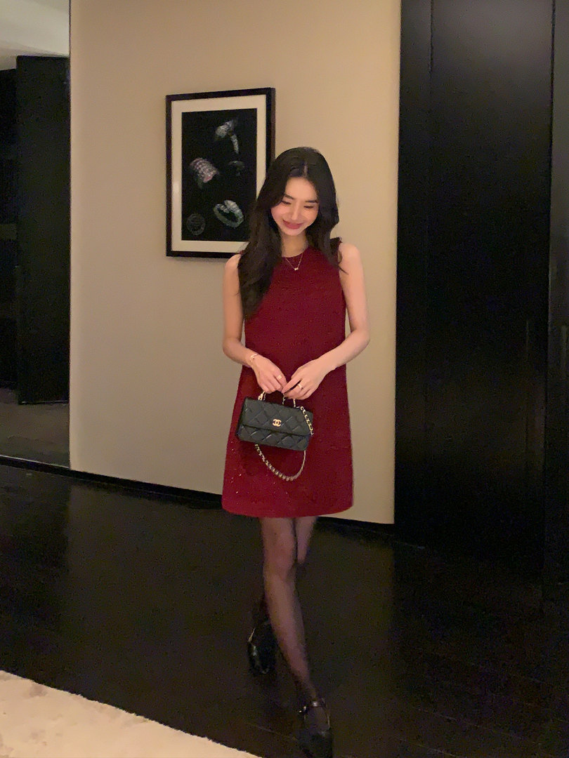 Woman wearing a sleeveless burgundy dress and holding a black quilted handbag