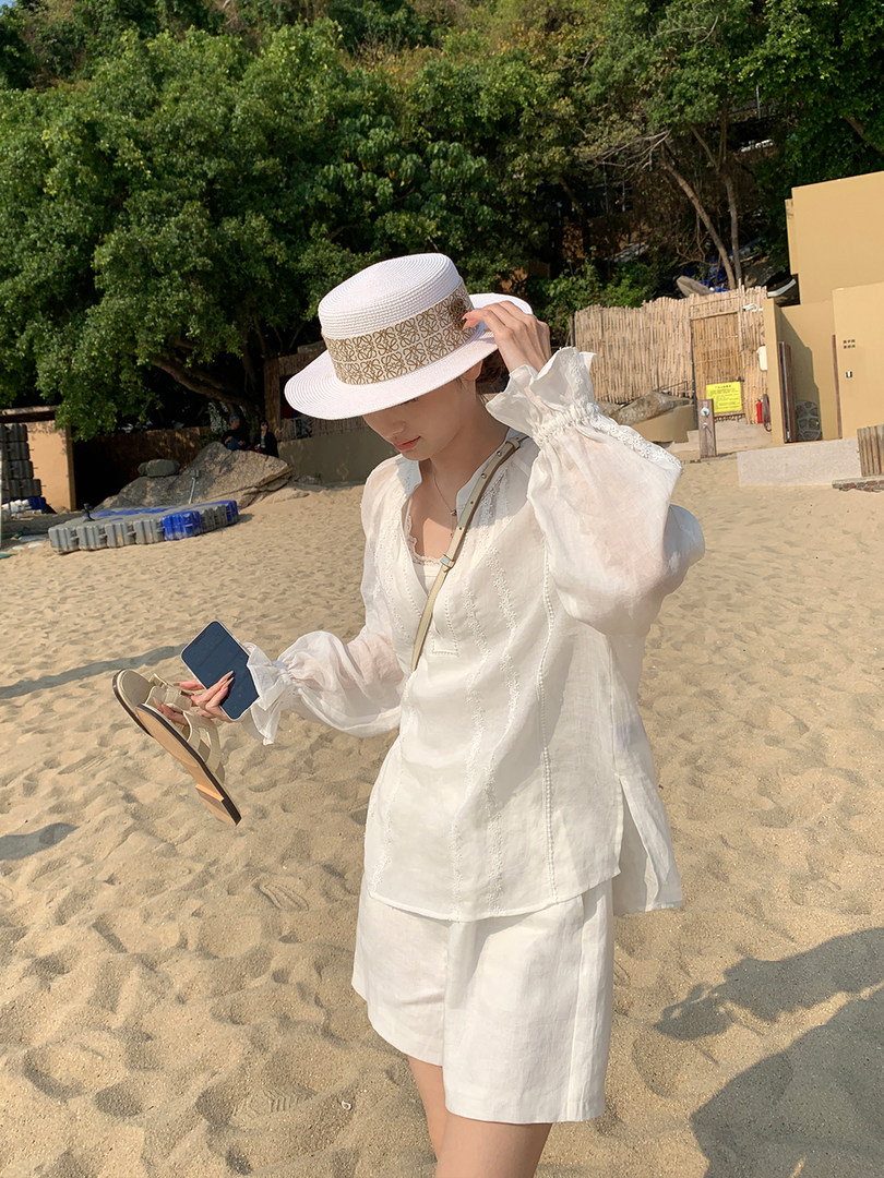 Woman wearing a white beach outfit with hat on the sand