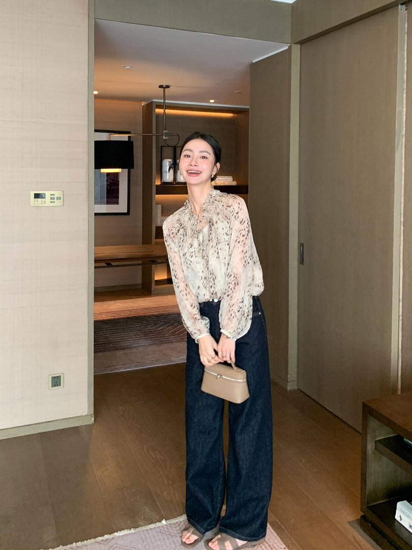 Woman wearing a sheer printed blouse with dark wide-leg jeans and a small beige handbag