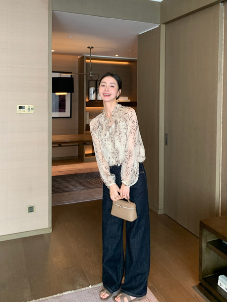 Woman wearing a sheer printed blouse with dark wide-leg jeans and a small beige handbag