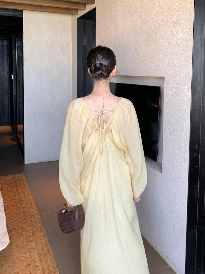 Woman wearing a pale yellow long-sleeve back-tie dress with a flowing silhouette