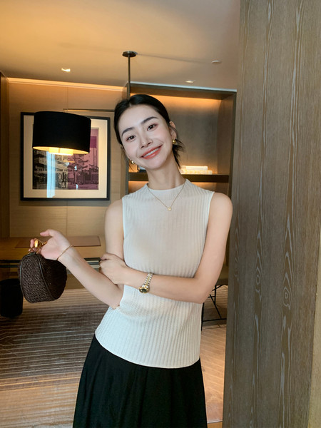 Woman wearing a sleeveless ribbed knit top and holding a small woven handbag
