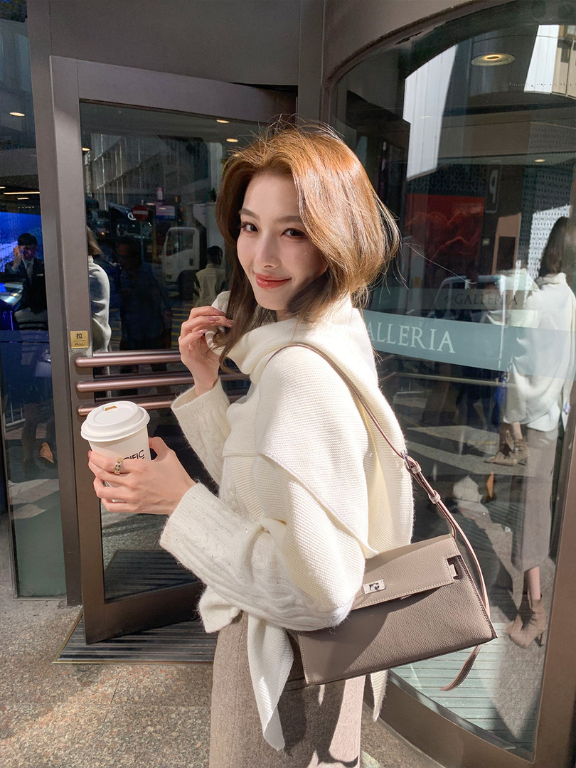 Woman wearing a cream sweater and carrying a taupe shoulder handbag outdoors