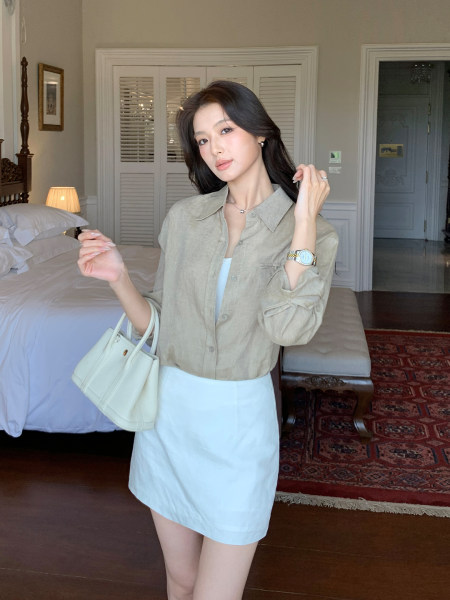 Woman wearing a beige button-up shirt with a white skirt and cream handbag