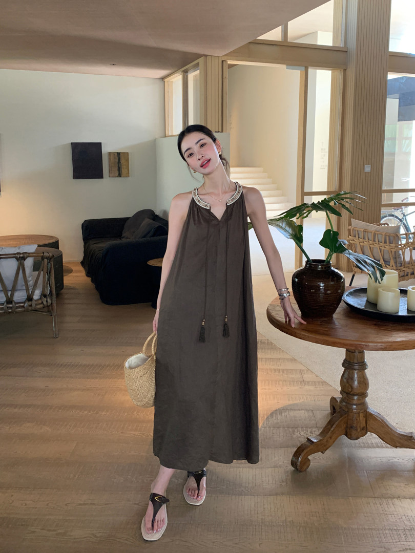 Woman modeling a dark sleeveless maxi dress with a woven bag in a bright interior setting