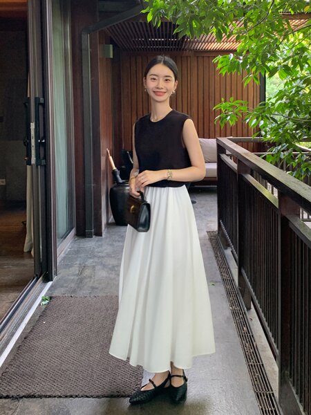 Woman wearing a black sleeveless top with a long white maxi skirt and black flats