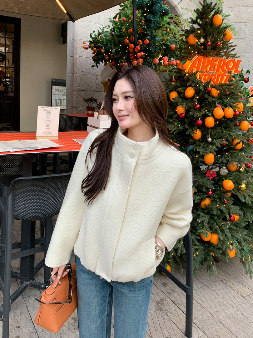 Woman wearing a cream button-front coat and holding an orange handbag outdoors