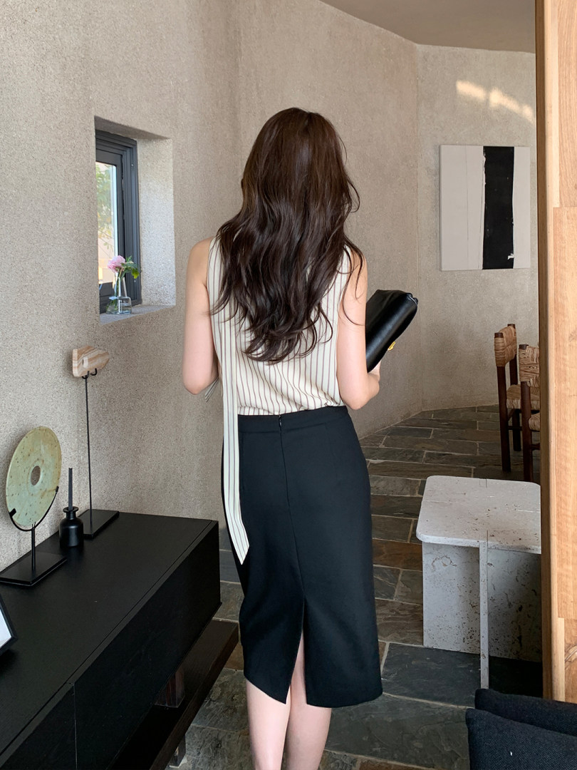 Model wearing a sleeveless striped top with a black midi skirt indoors
