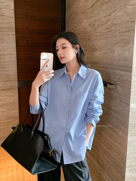 Model wearing a light blue oversized button-up shirt with a black handbag