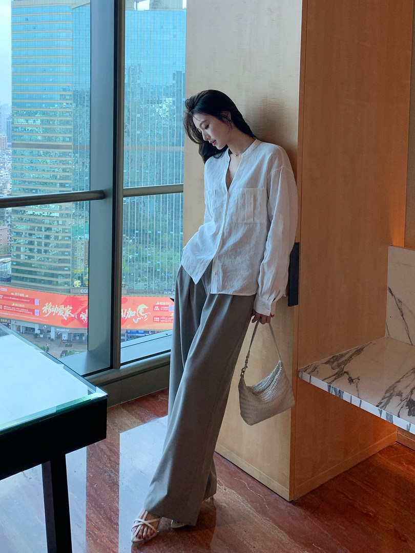 Woman wearing a white blouse, gray wide-leg pants, and holding a small handbag