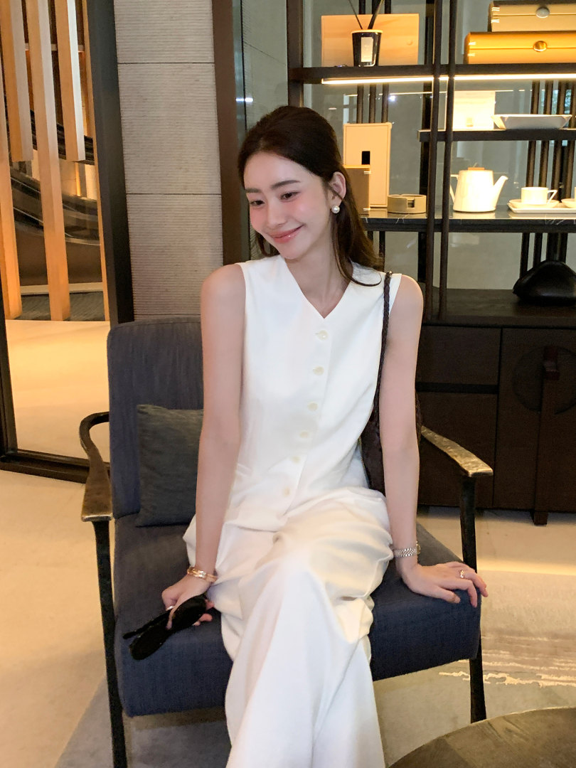 Woman wearing a white sleeveless button-front outfit seated indoors