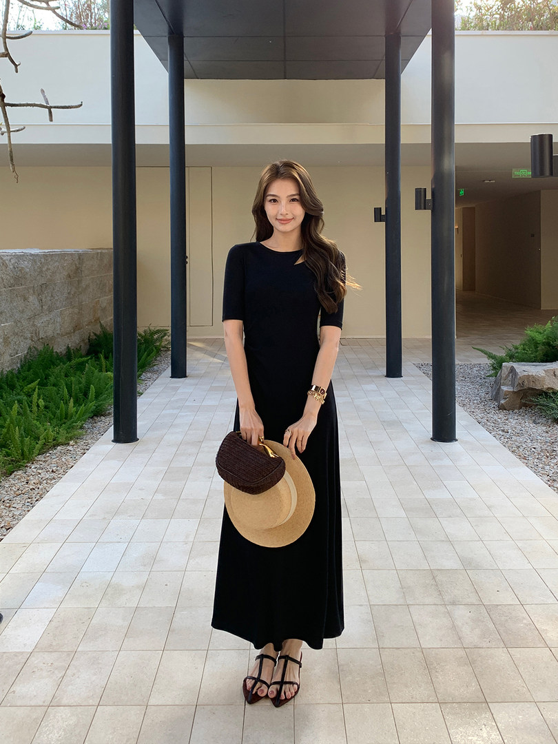 Woman wearing a black maxi dress with short sleeves and holding a hat