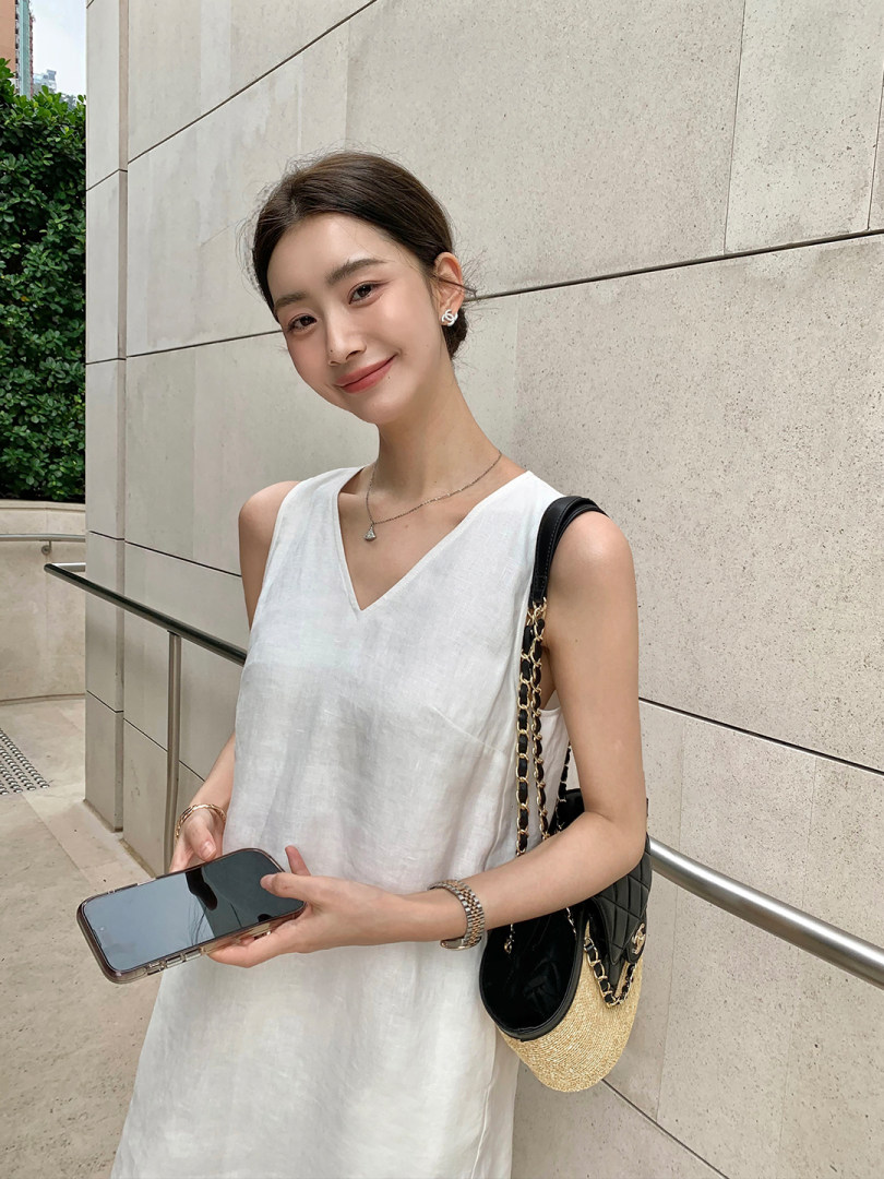 Woman wearing a white sleeveless dress and carrying a black chain-strap handbag