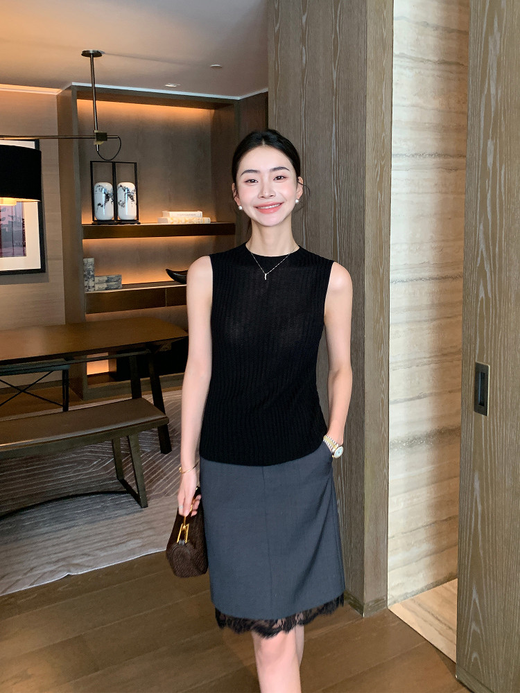 Woman wearing a black sleeveless knit top with a gray skirt indoors