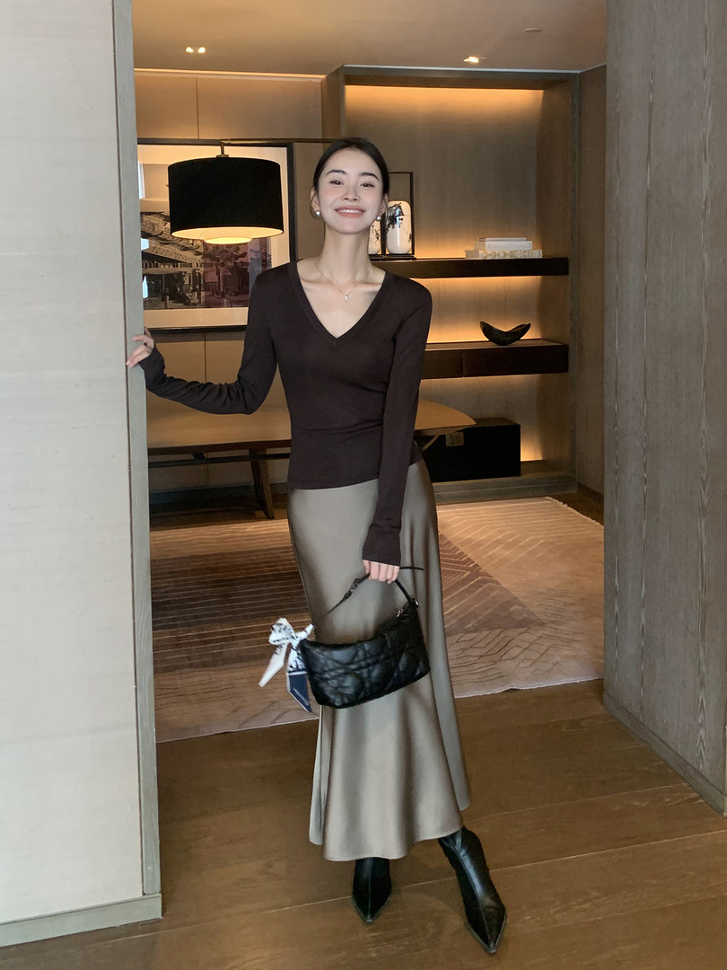 Woman modeling a black long-sleeve top with a satin midi skirt and black handbag