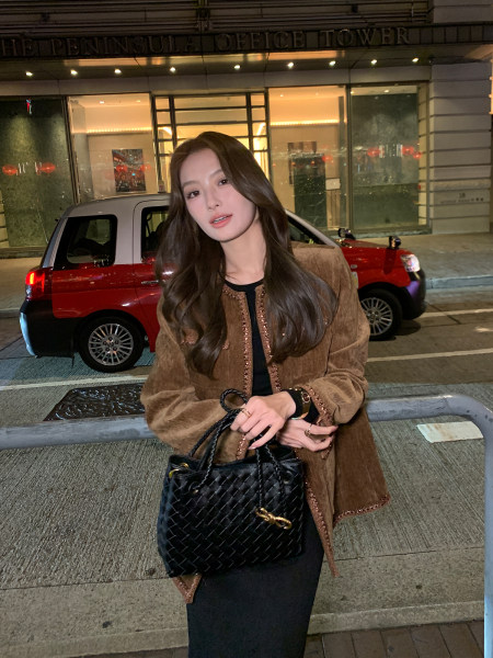 Woman wearing a brown jacket and black outfit while holding a black quilted handbag at night