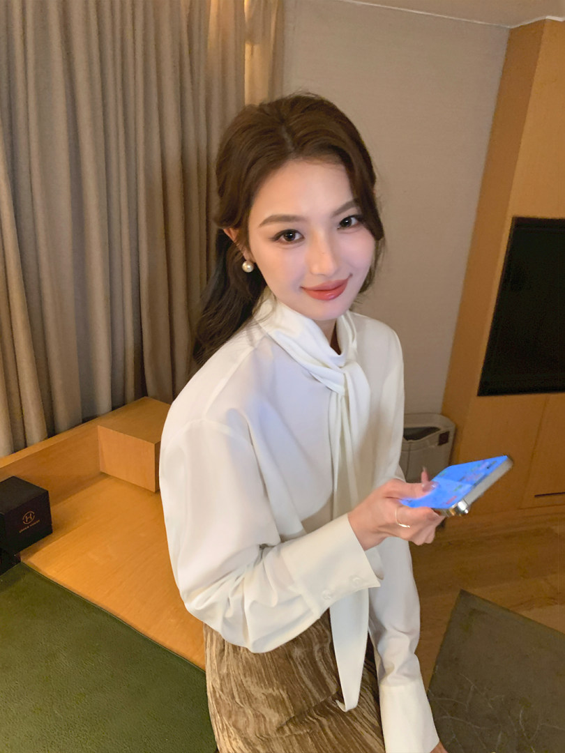 Woman wearing a white tie-neck blouse with a brown velvet skirt indoors