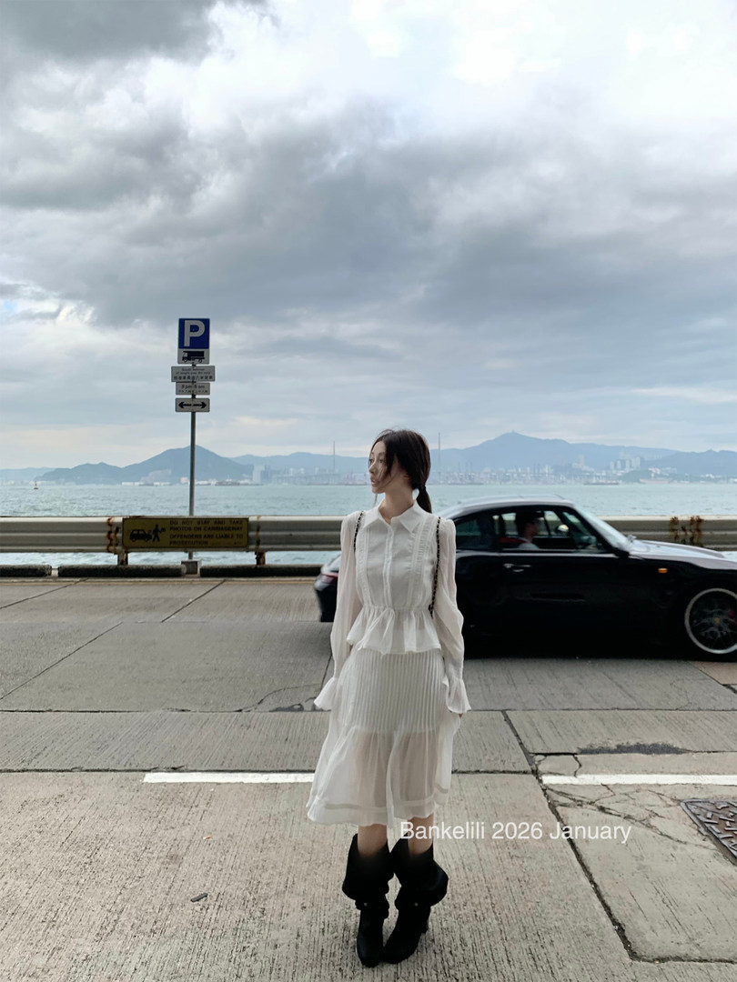 Woman wearing a sheer white dress with black boots by the waterfront