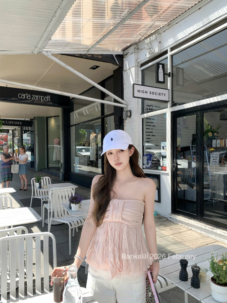 Woman wearing a pale pink strapless top with white pants and a white cap at a cafe