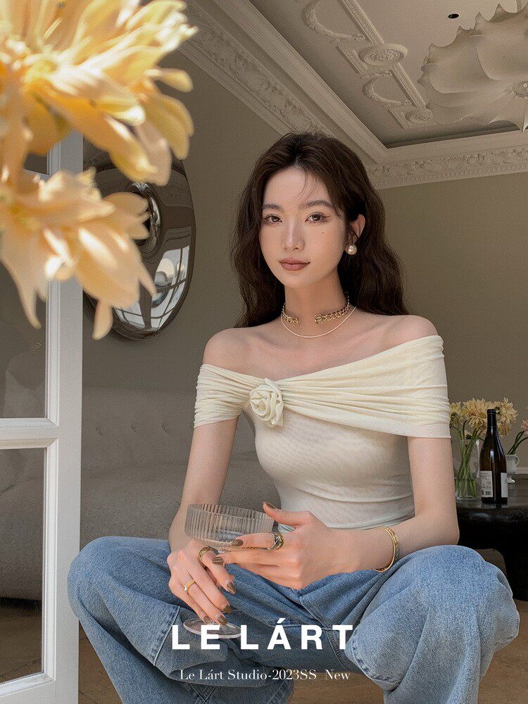 Woman wearing a cream off-shoulder top with a floral detail and blue jeans