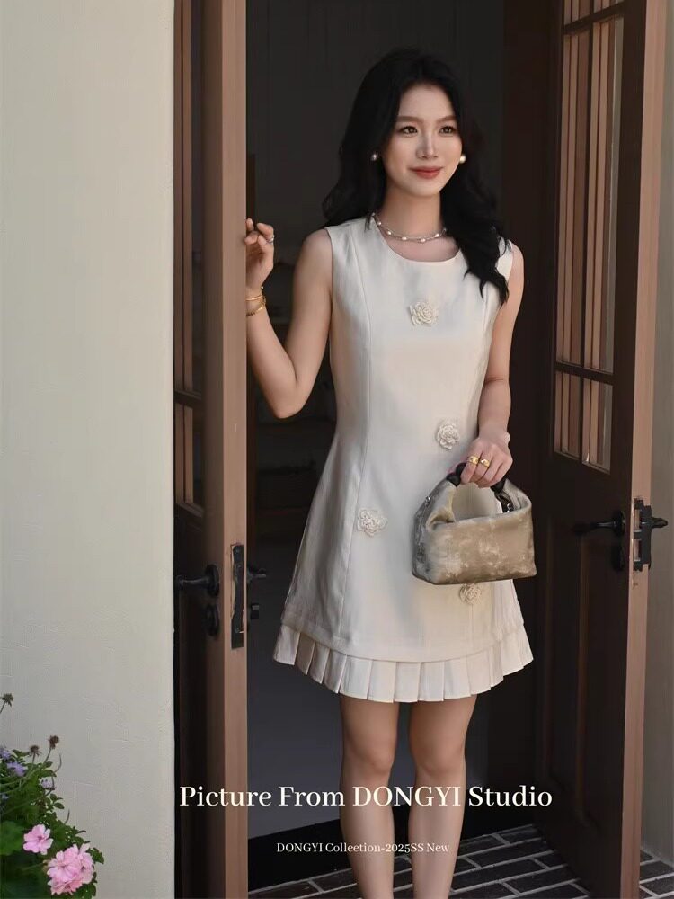Woman wearing a cream sleeveless dress with pleated hem and holding a small handbag