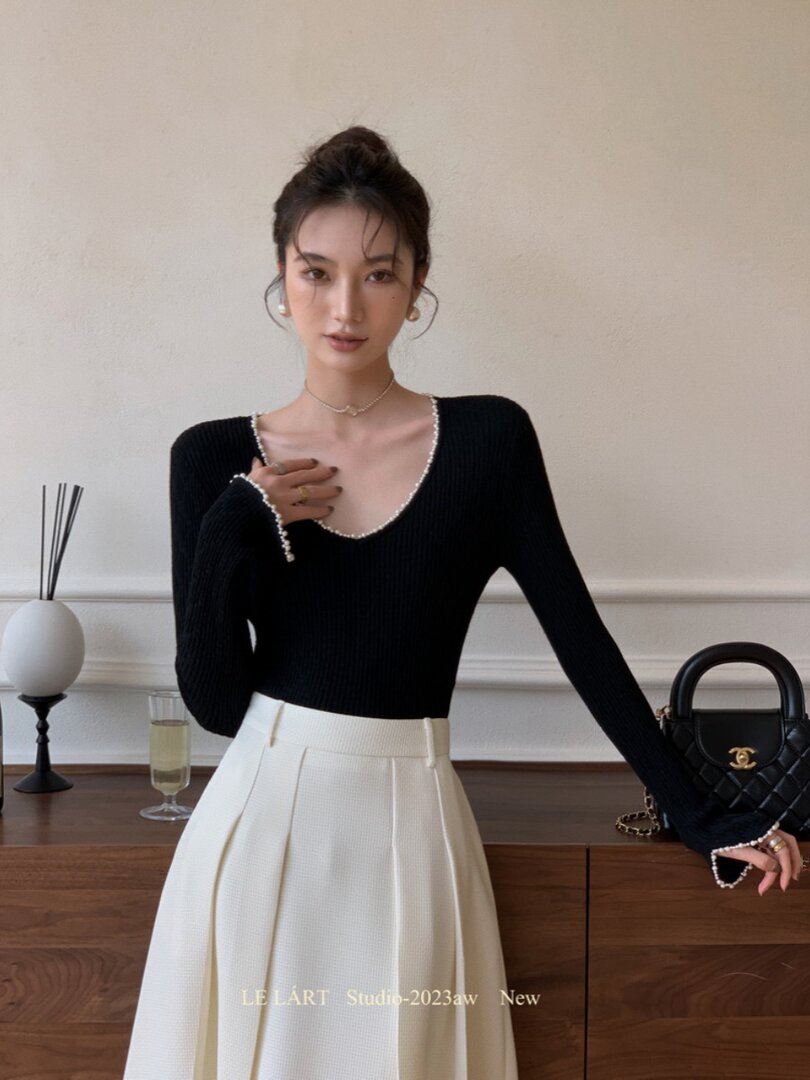 Model wearing a black long-sleeve top with pearl trim and a white pleated skirt