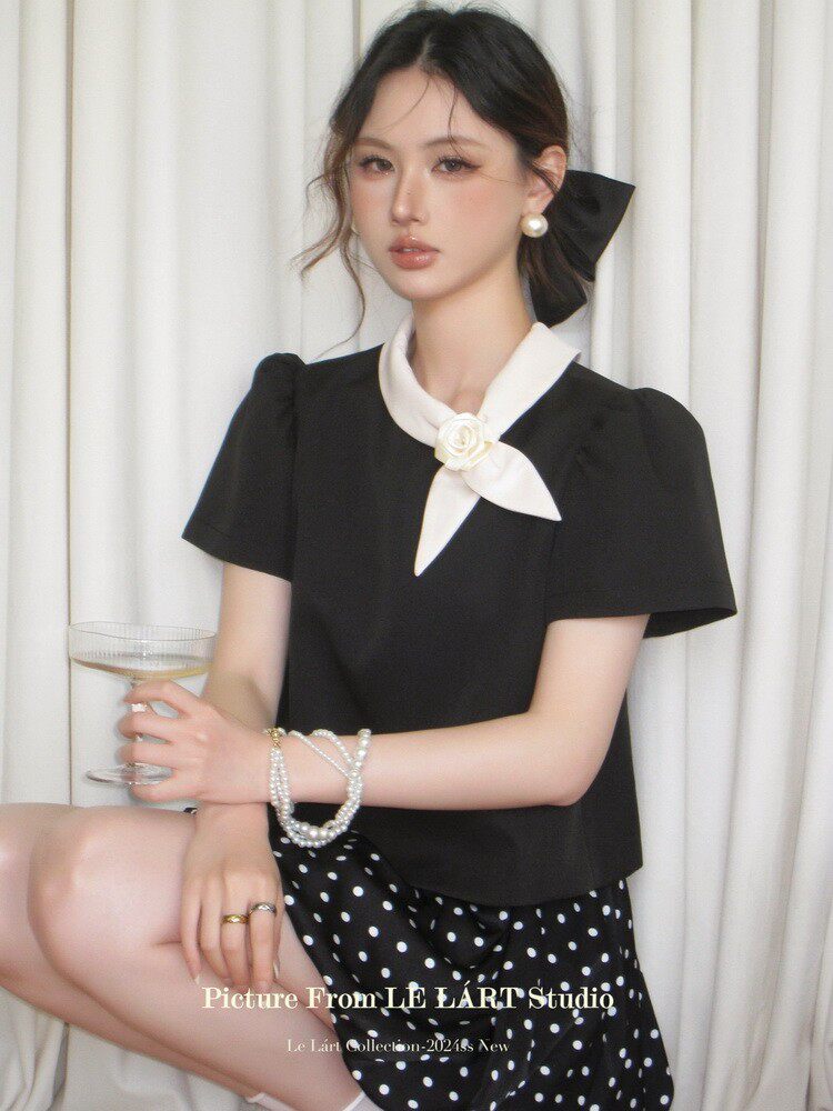 Black short-sleeve blouse with a white scarf tie detail, worn by a model