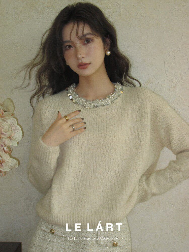 Model wearing a cream knit sweater with embellished neckline
