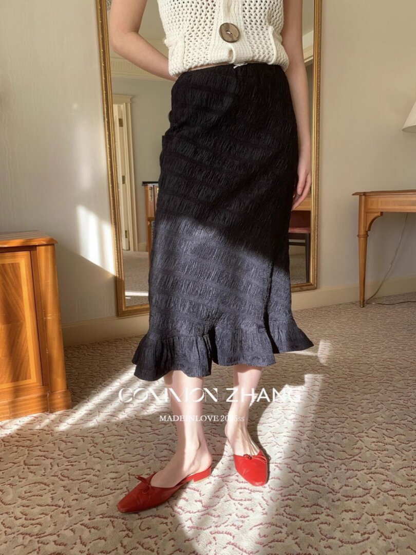Model wearing a black textured midi skirt with ruffled hem and red slip-on shoes