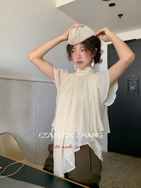 Model wearing a cream draped sleeveless blouse with a matching hat