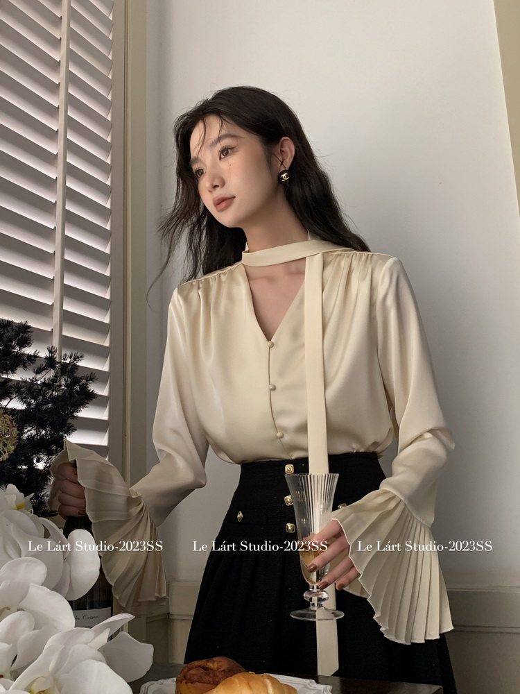 Model wearing a cream long-sleeve blouse with a black skirt