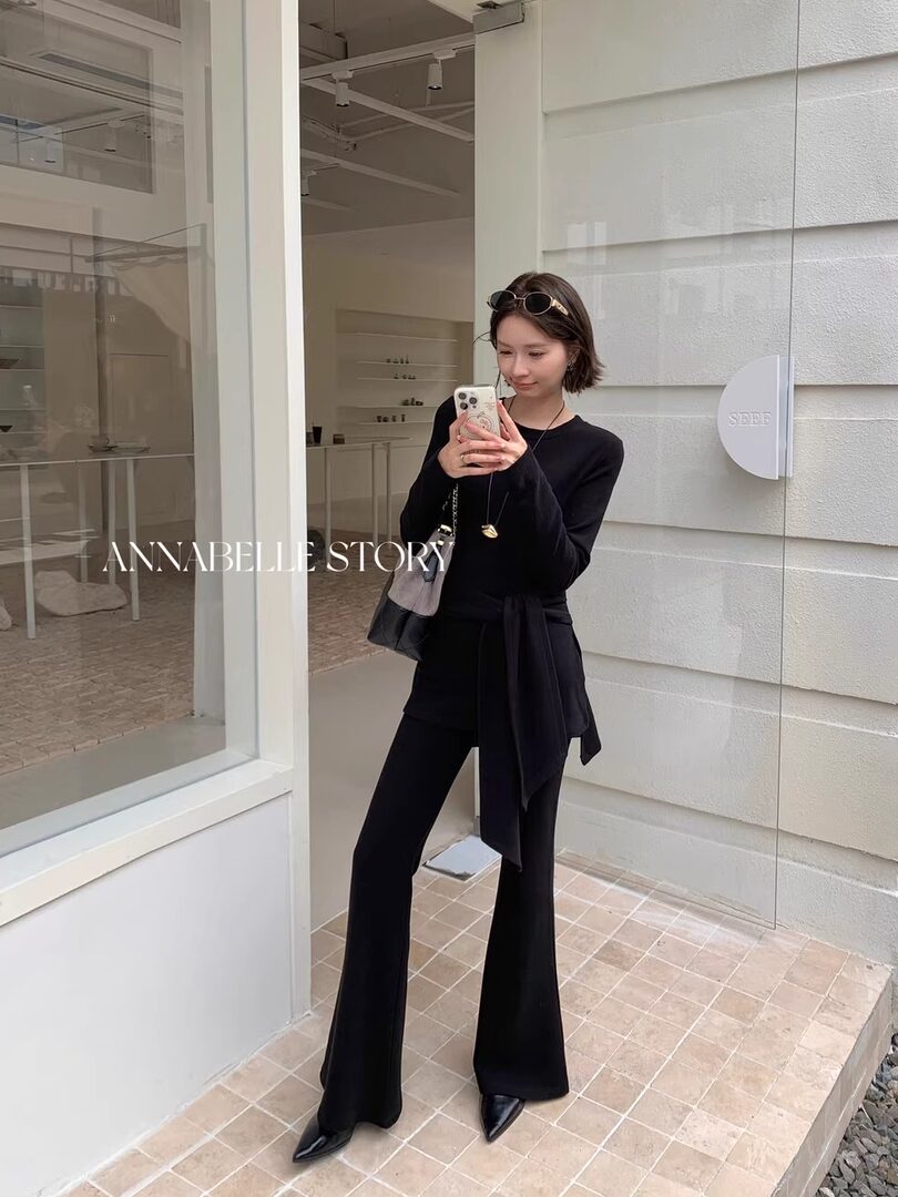 Woman wearing a black long-sleeve top and flared pants in a mirror selfie