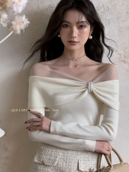 Model wearing an off-shoulder cream knit top with sheer neckline detail