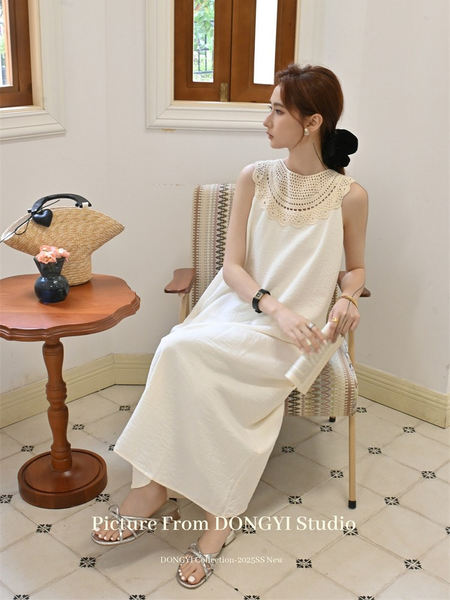 Woman wearing a white sleeveless lace-collar dress seated indoors