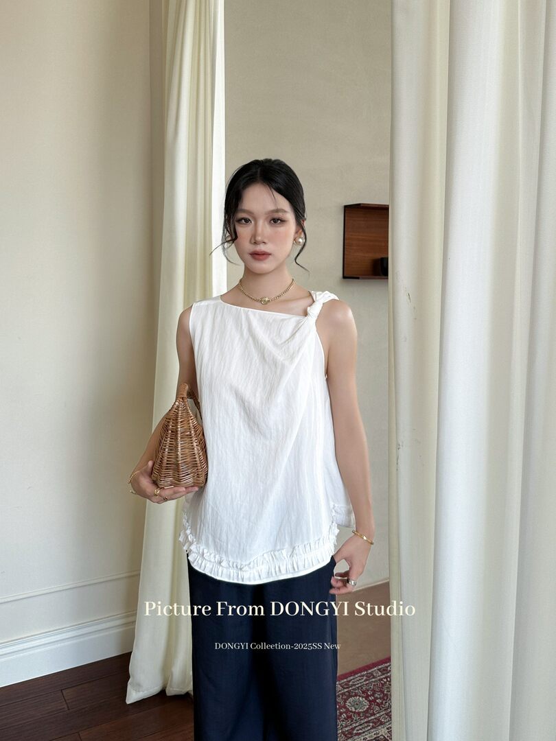 White sleeveless top worn by a model with a woven handbag