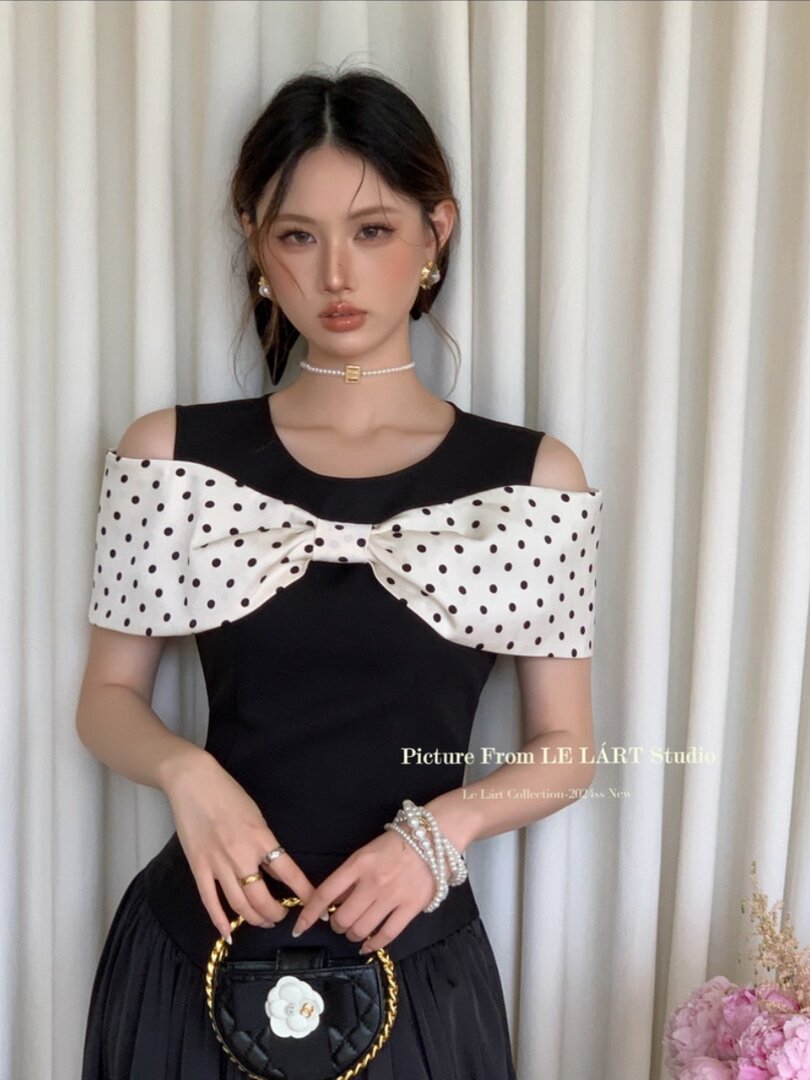 Black off-shoulder dress with a large white polka-dot bow worn by a model
