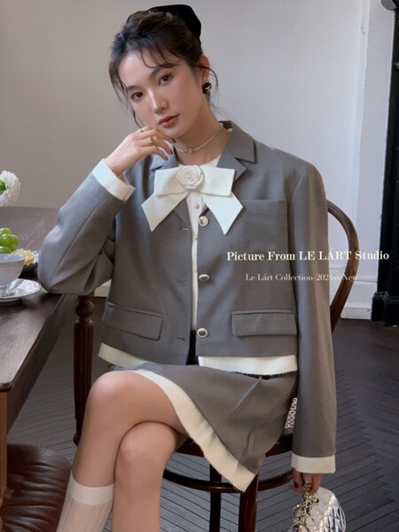 Woman wearing a gray blazer and matching skirt outfit with white bow detail