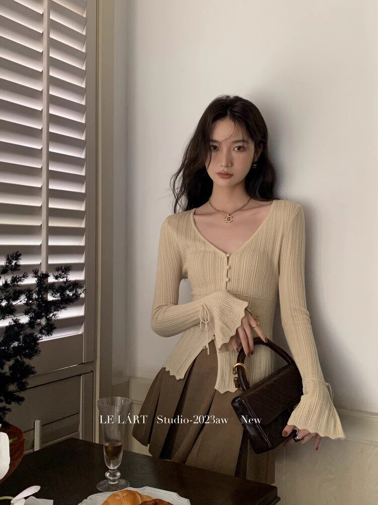 Model wearing a beige ribbed knit top with a brown pleated skirt and dark handbag
