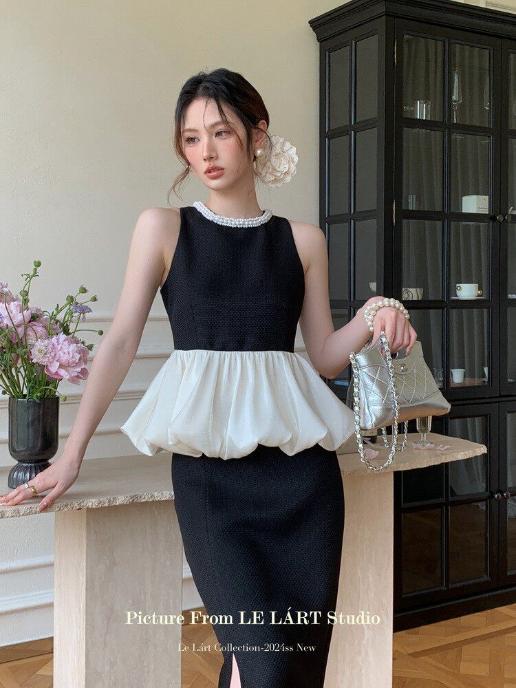 Black and white sleeveless dress worn by a model, styled with pearl details and a small handbag