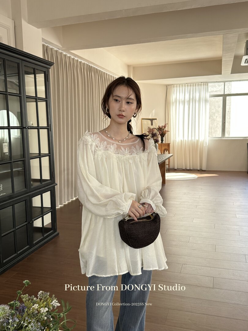 Woman wearing a white embroidered sheer blouse with blue jeans and a small woven handbag