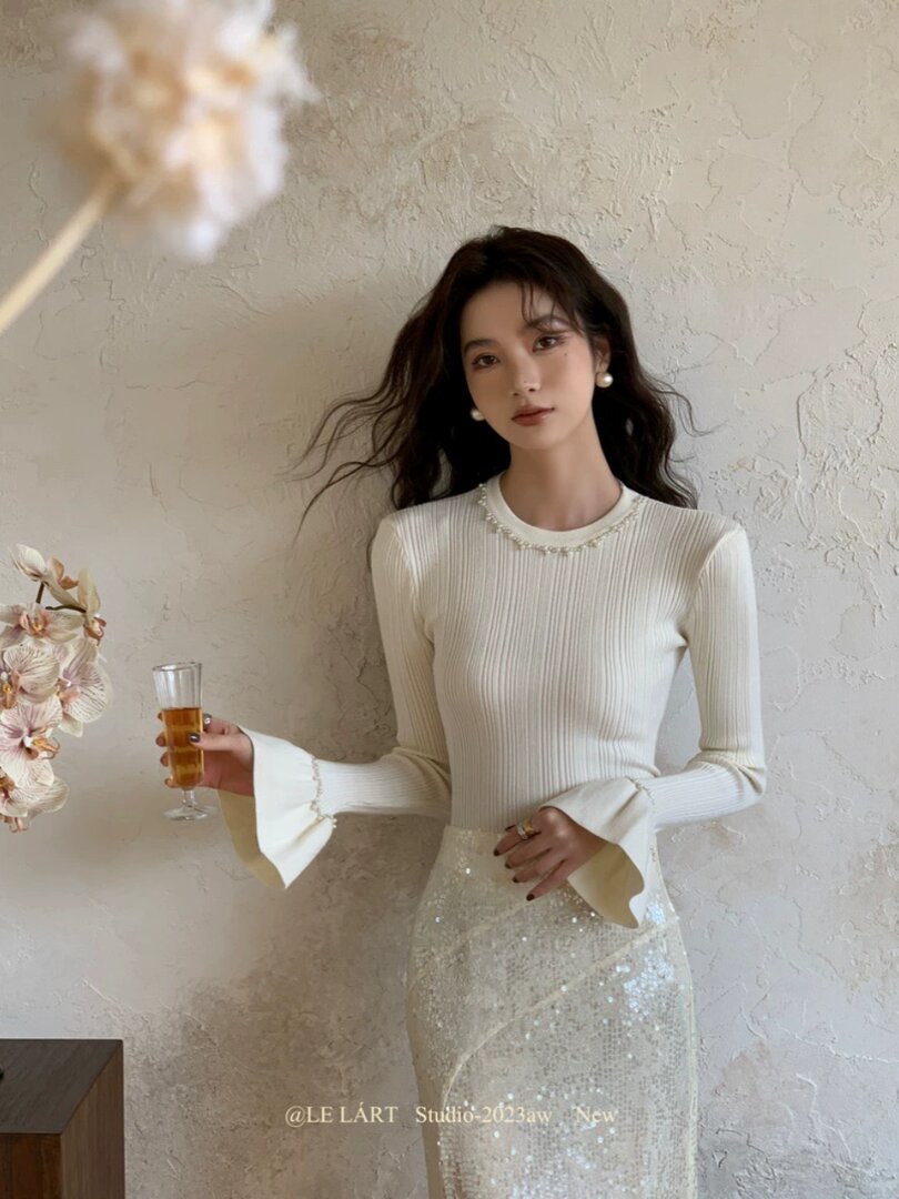 Woman wearing a white ribbed top with flared sleeves and a sparkly skirt