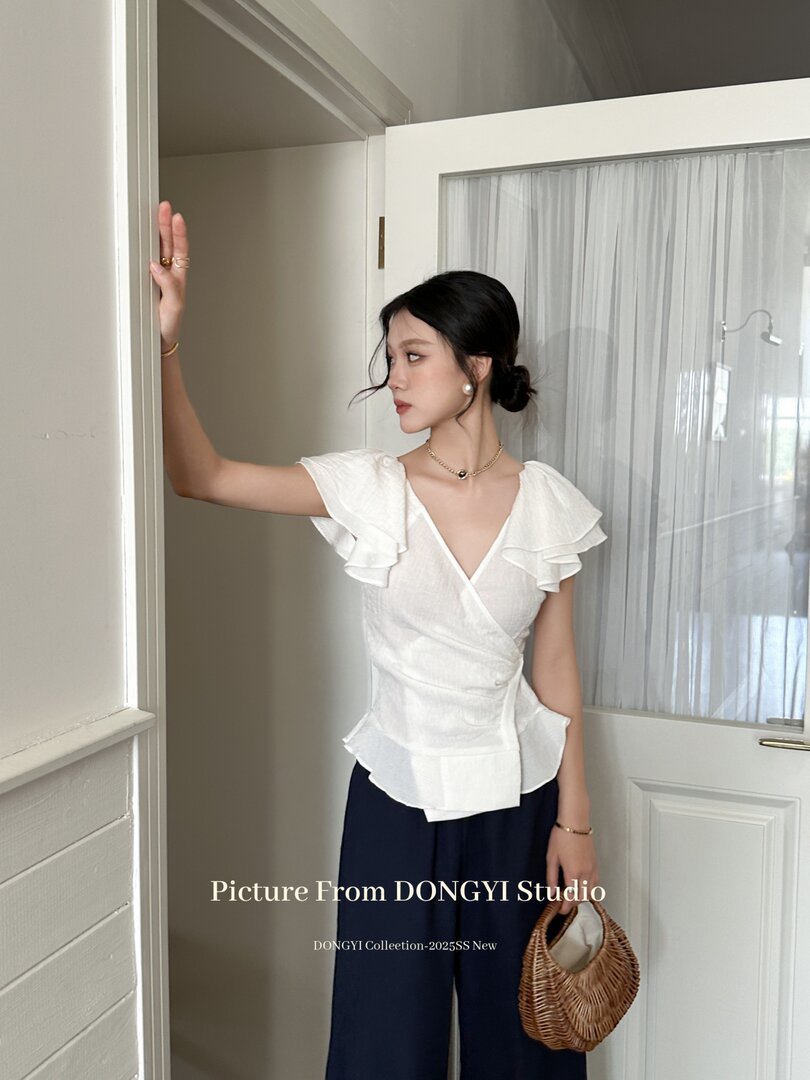 Woman wearing a white ruffled V-neck blouse with navy pants and a woven handbag