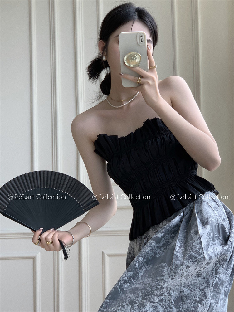 Model wearing a black strapless top with a patterned skirt and holding a black fan